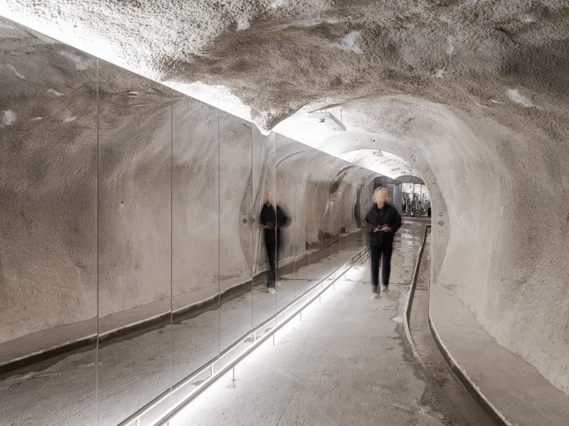 Curved ice tunnel with polished rock walls, glass balustrade, and recessed rail lighting