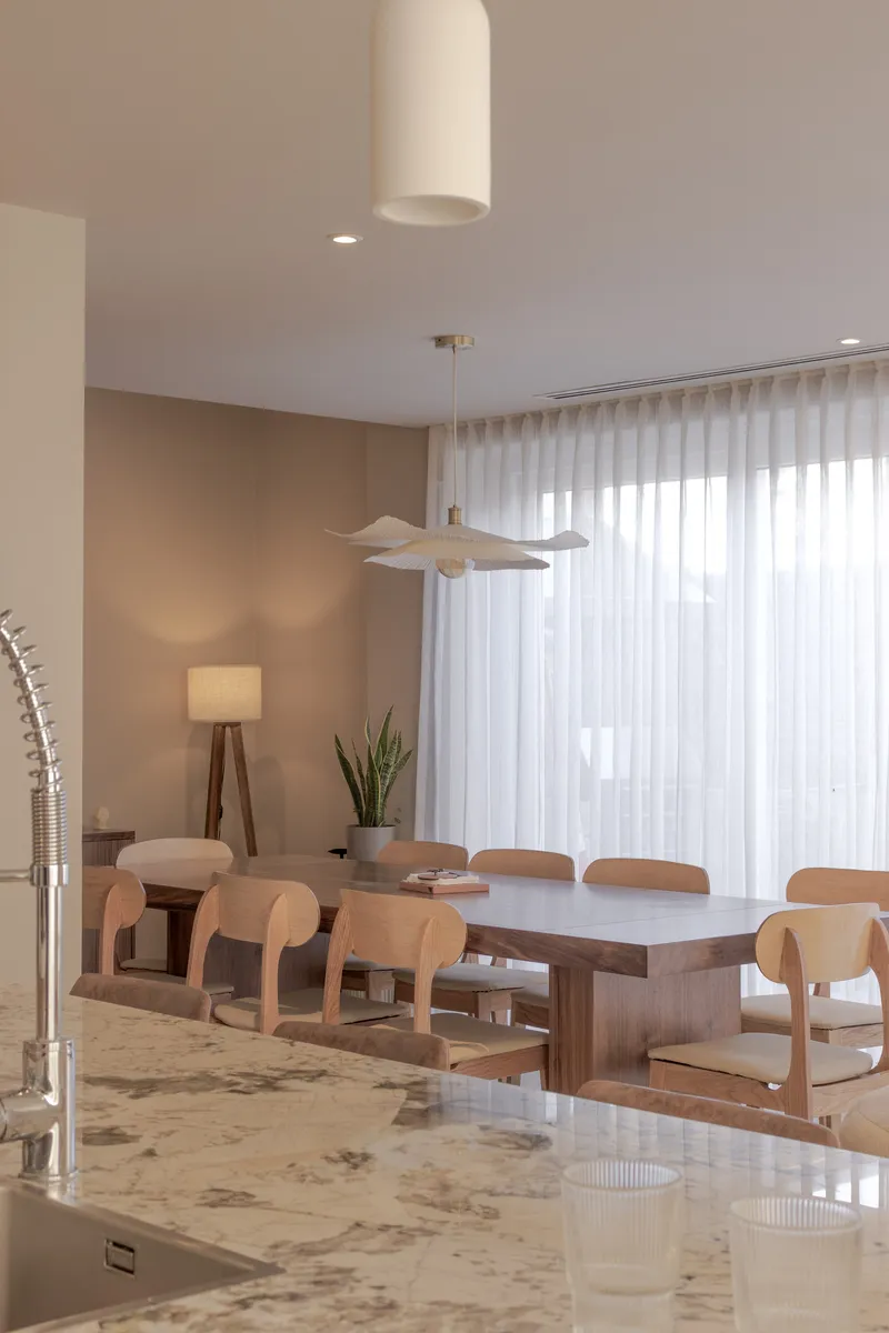 Dining area with timber table, curved-back chairs and sheer curtains filtering soft daylight