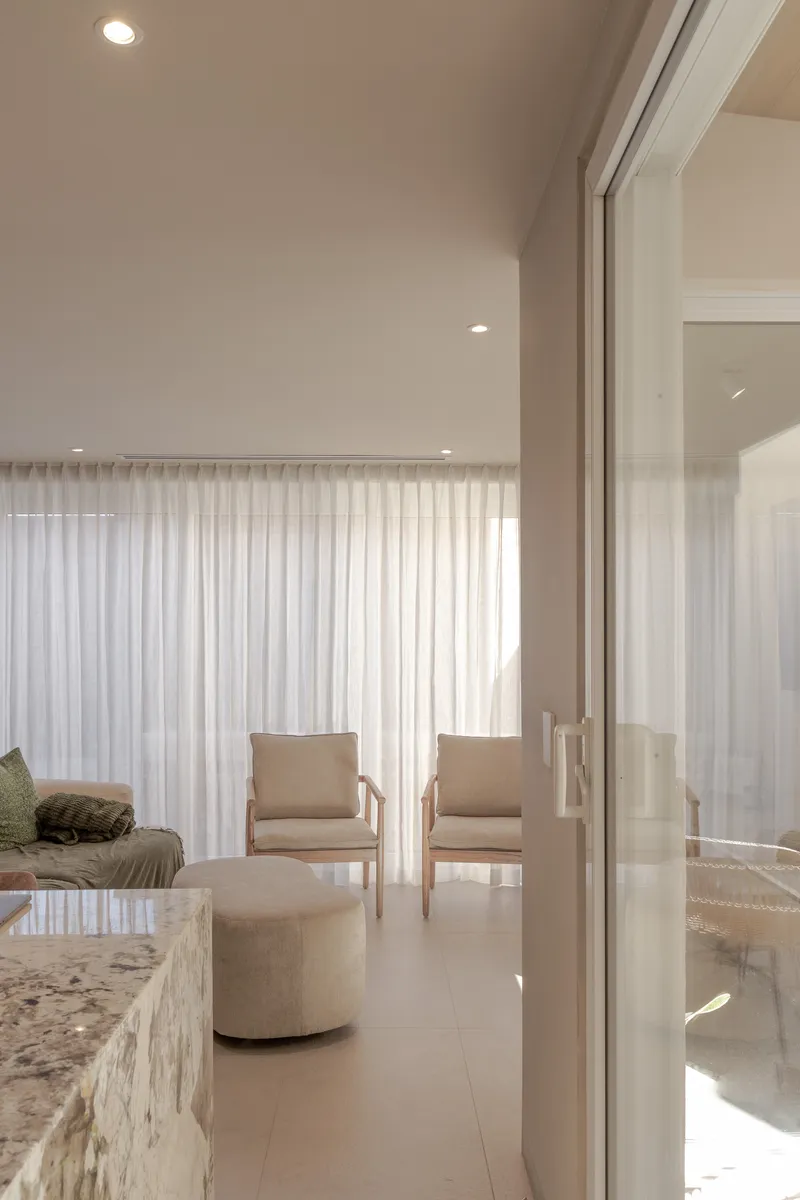 Living room with sliding glass door, upholstered chairs and floor-to-ceiling sheer drapes