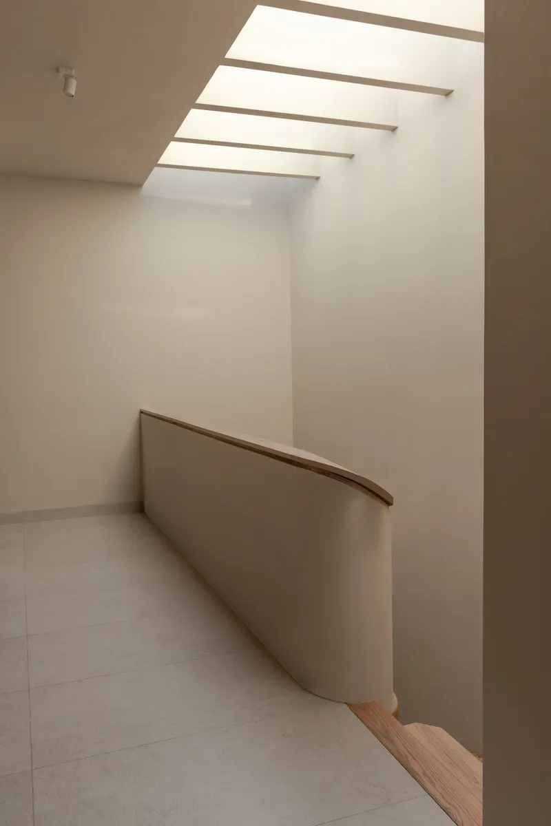 Curved timber handrail along a stair landing under a clerestory with horizontal beams