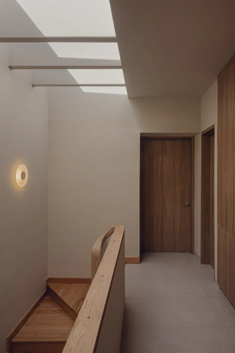 Upper hallway with timber doors and a wall sconce beneath a slatted skylight