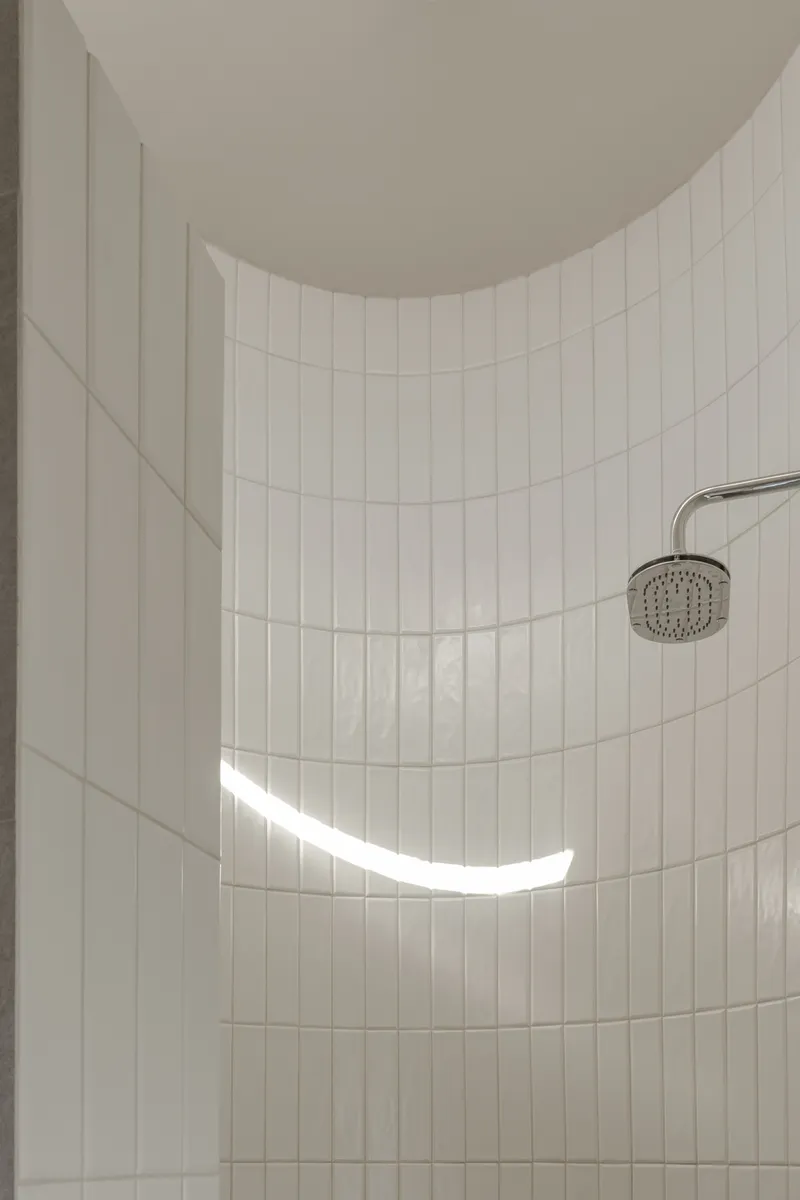 Curved white tile wall in shower with a thin horizontal window casting daylight