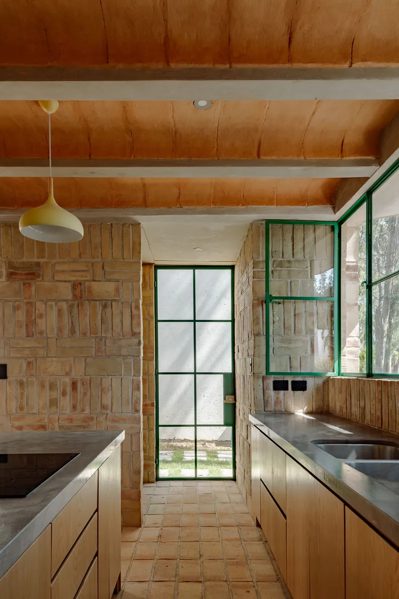 Galley kitchen with timber cabinetry, concrete countertops, and exposed ceiling beams lit by a pendant fixture