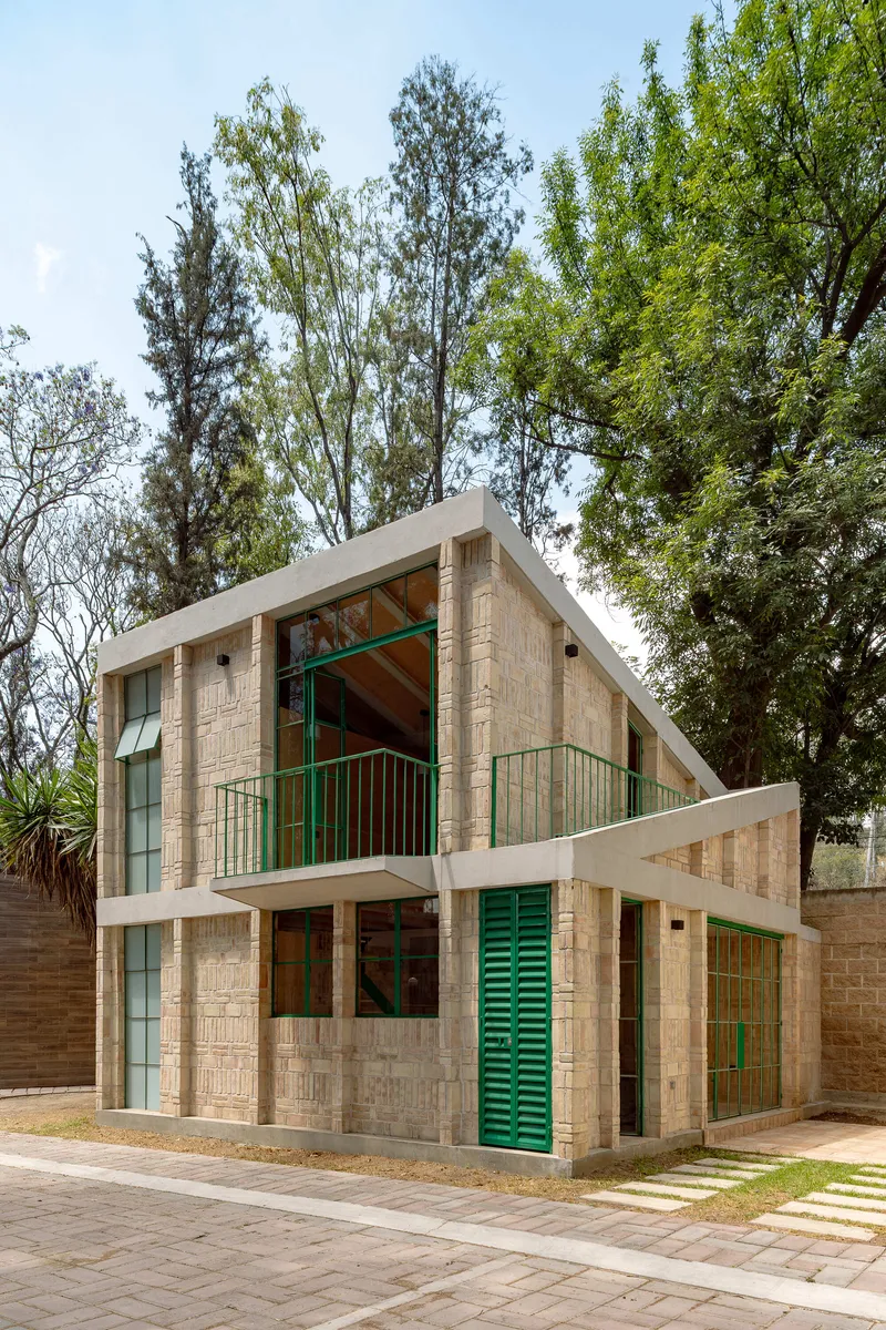 Street view of the two-story textured brick house with green shutters and balcony among tall trees