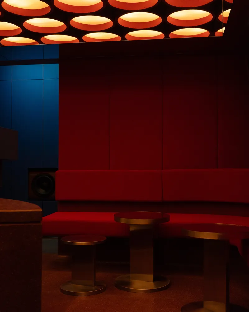 Red banquette seating beneath a ceiling grid of circular orange pendant lights