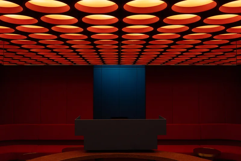 Interior view of the grid of circular orange ceiling lights above a black display counter in a red room