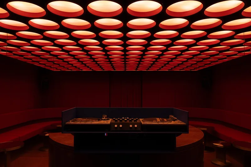 Central display counter with circular orange ottomans beneath the illuminated ceiling grid in the red interior
