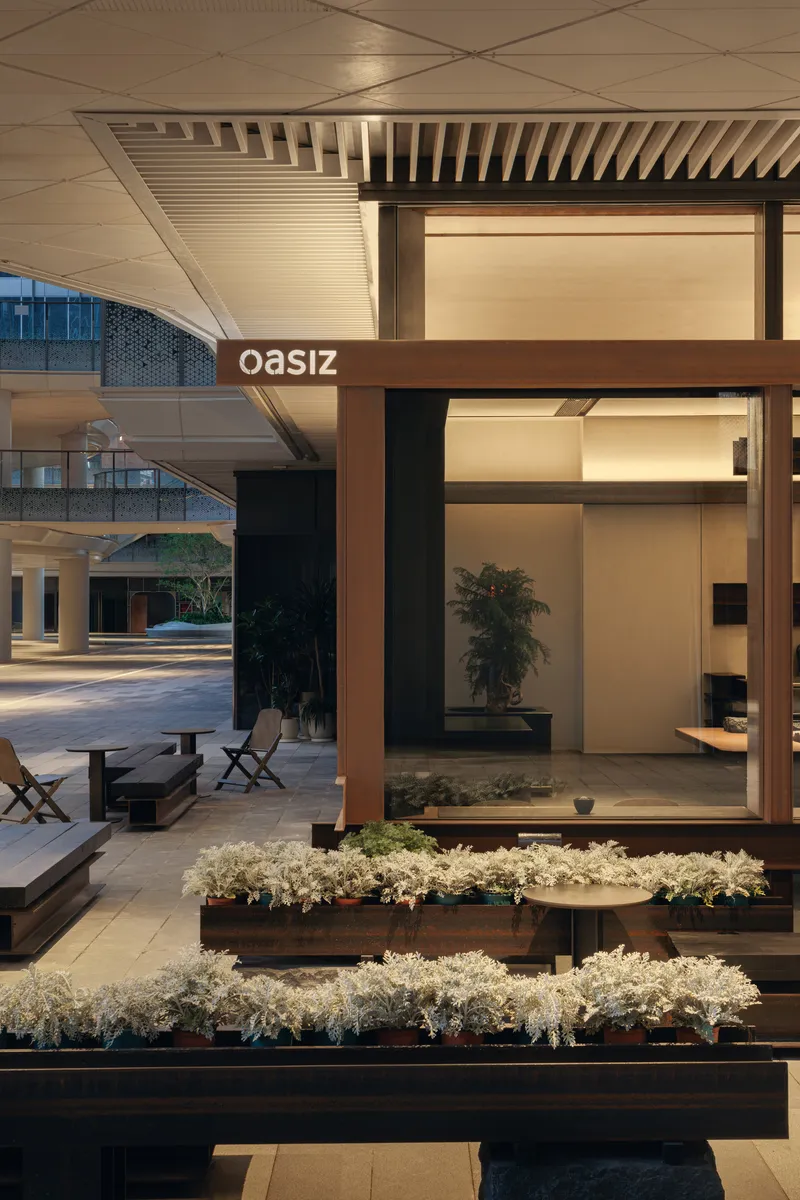Glass-walled pavilion with timber frame and planted beds of white flowering groundcover at dusk