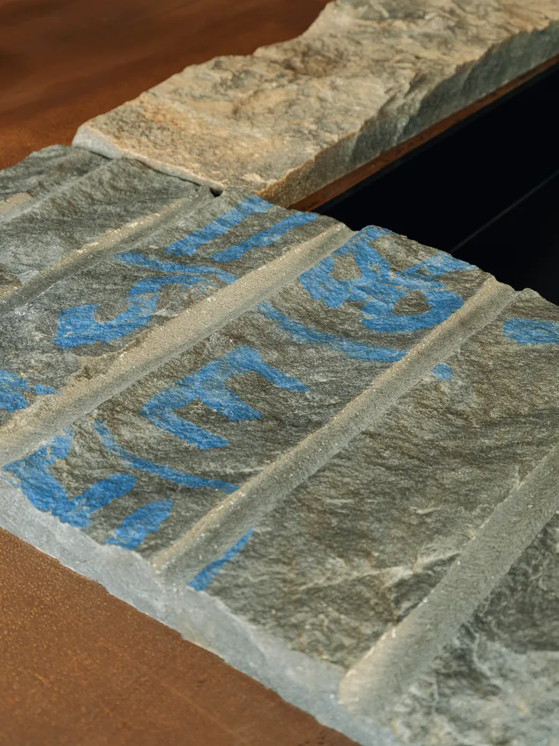 Close-up of carved stone panels with blue painted lettering and textured surface