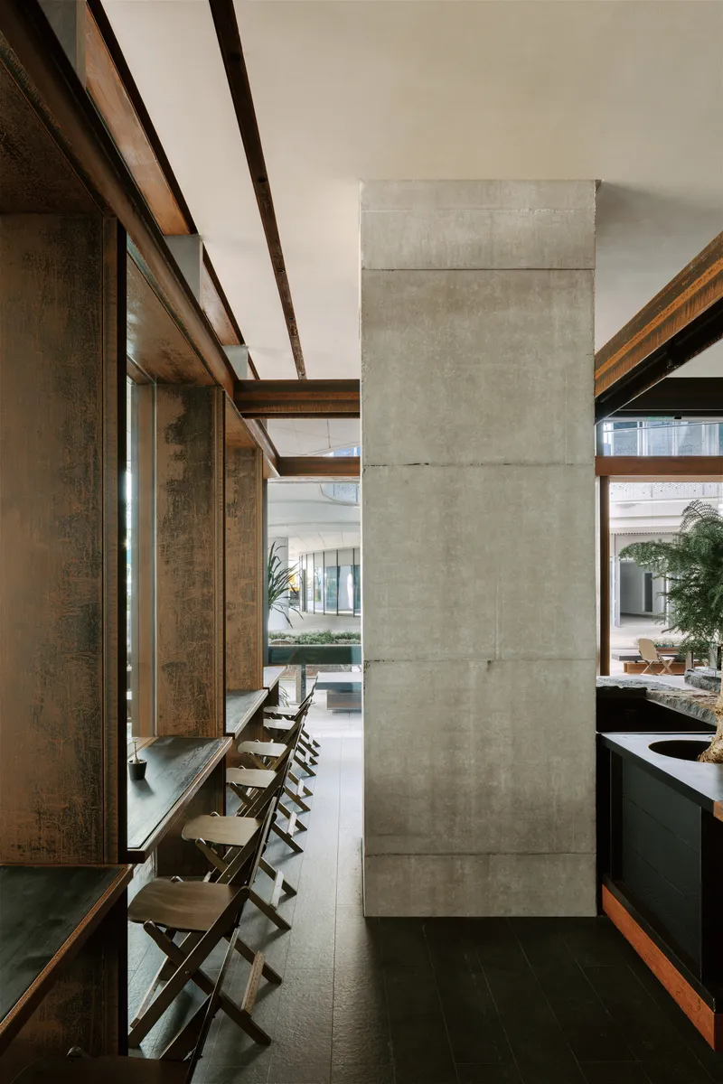 Poured concrete column beside a timber-framed wall with folding chairs along a narrow ledge