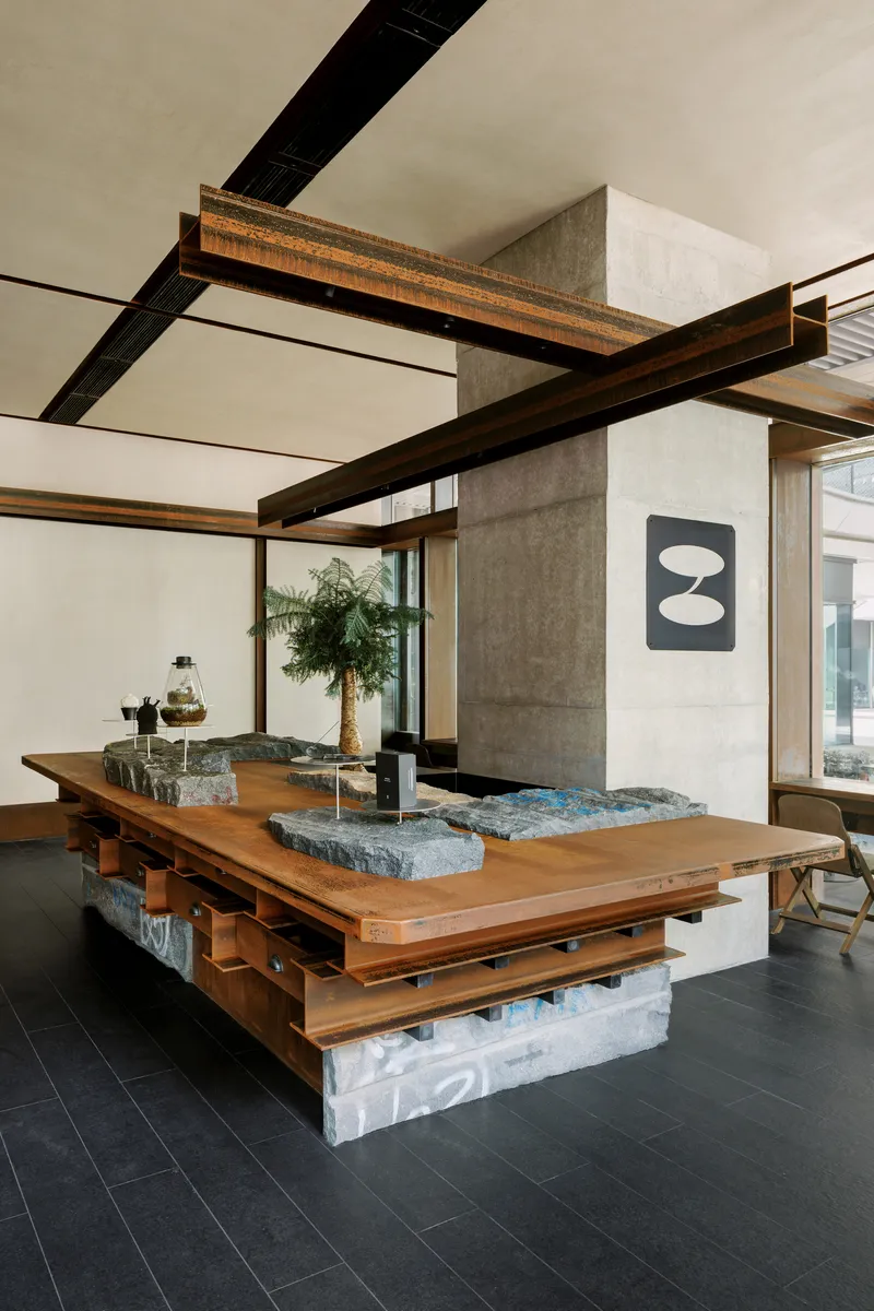 Central communal table with timber frame and embedded granite stone slabs on dark tile floor