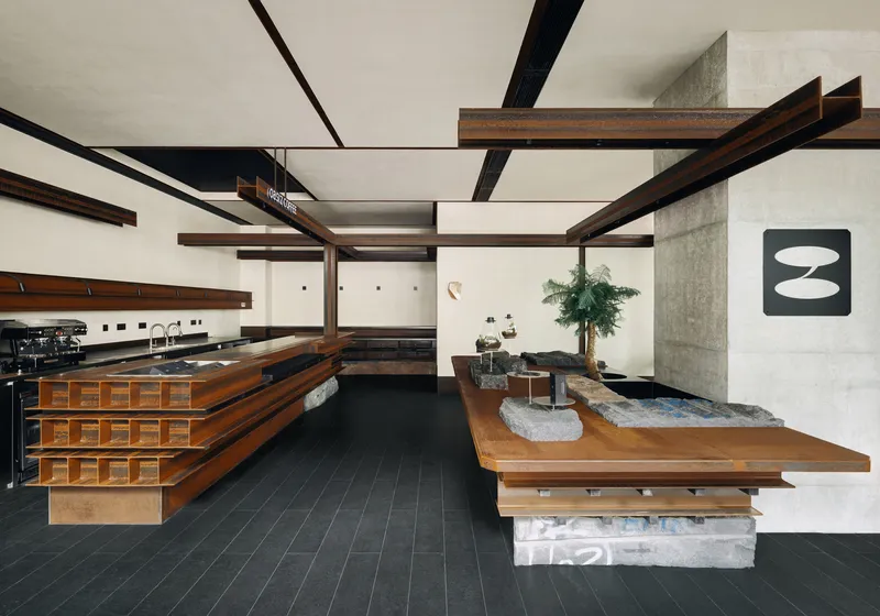 Interior cafe space with dark timber counters, exposed beams, and black tile flooring beneath white stretched fabric ceiling