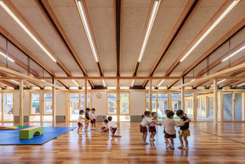 Open classroom space with timber beams and integrated linear lighting as children gather on the floor