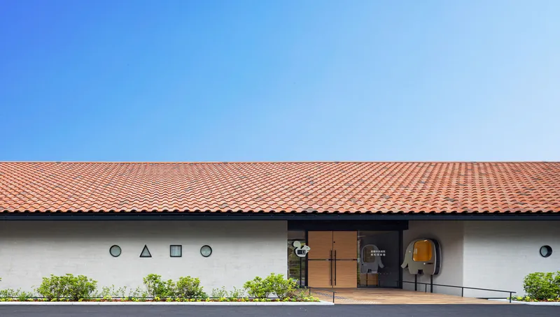 Entrance facade with geometric window openings in white stucco beneath the red tile roof