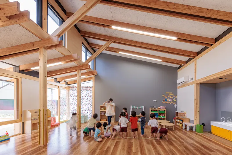 Classroom with exposed timber beams and ceiling panels where children gather on the wood floor