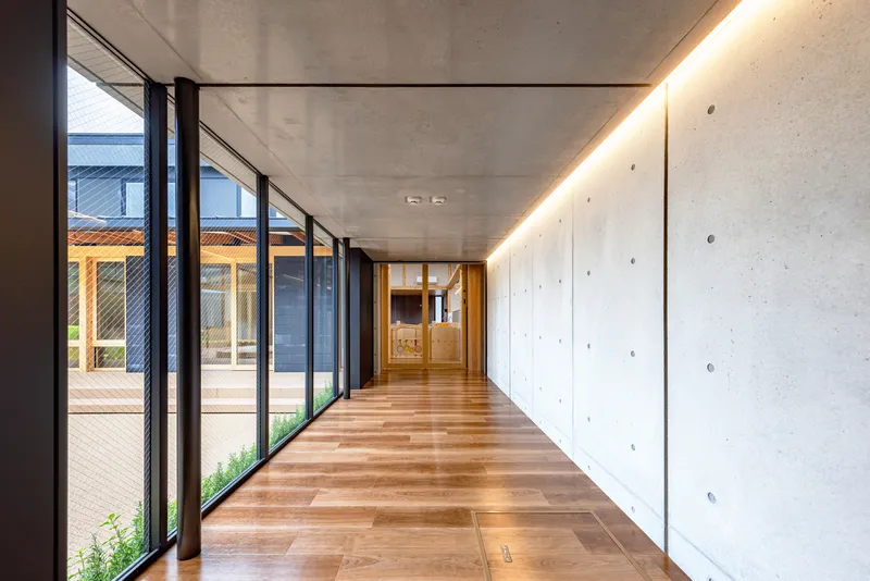Corridor with poured concrete wall and recessed linear ceiling lighting alongside glazed courtyard doors