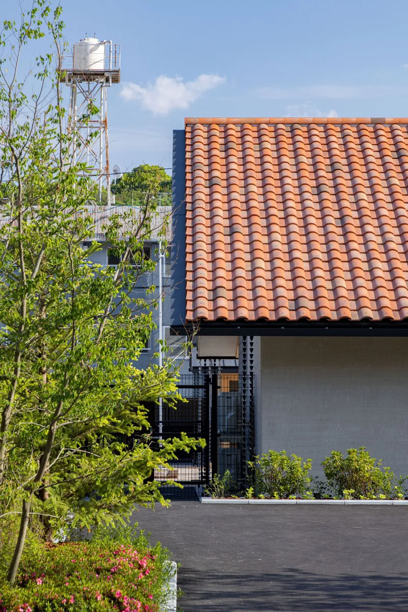 Orange clay tile roof with a planted bed of young trees and a water tower in the background