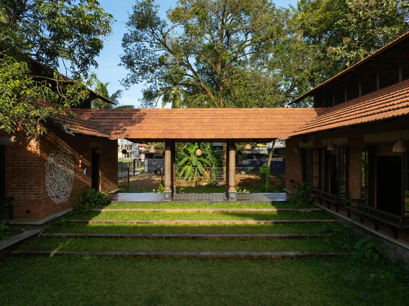 Open pavilion with timber posts and clay tile roof spanning between brick volumes and lawn