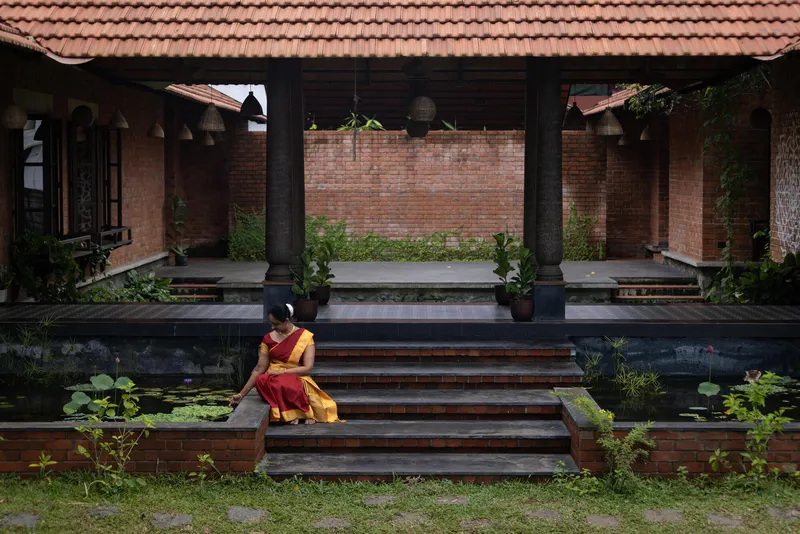 Person in red and yellow seated on dark brick steps beside a lily pond
