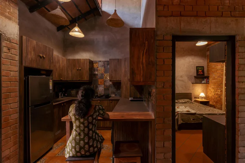 Kitchen with timber cabinetry and terracotta tile wall as a woman prepares food under pendant lights