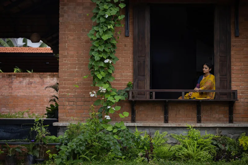 Brick veranda with timber bench where a woman sits beside climbing vines and lush garden plantings