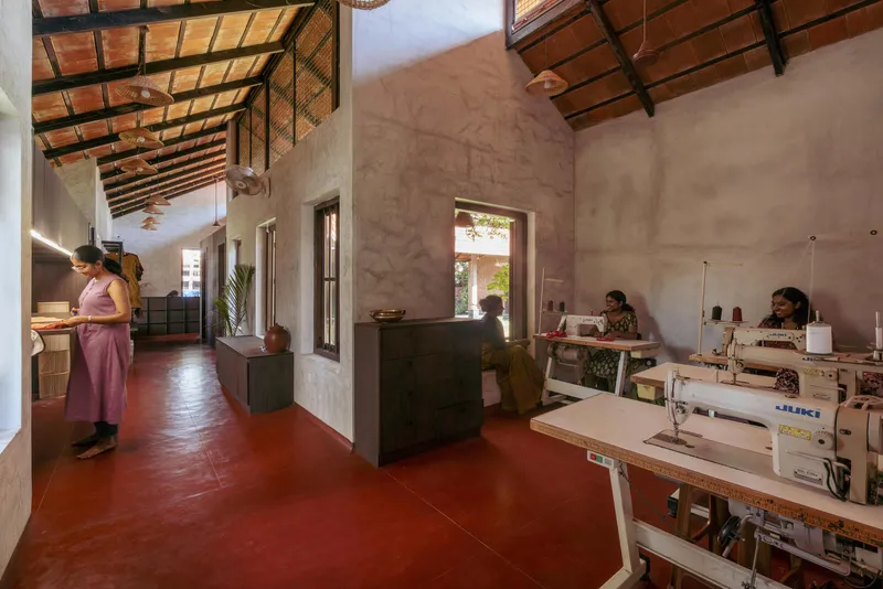 Workshop interior with red oxide floor and exposed timber rafters where women operate sewing machines
