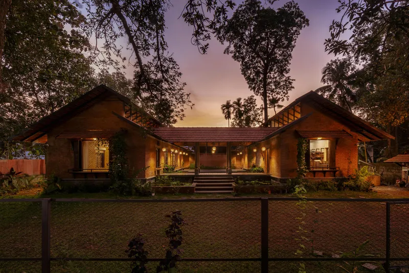 Symmetrical facade with two gabled brick wings flanking a central breezeway under overhanging trees at dusk