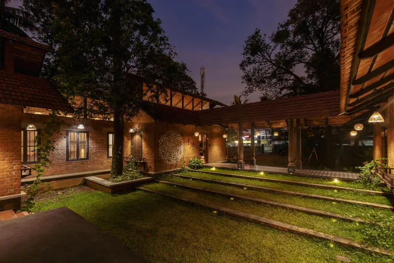 Central courtyard with grass strips and raised planters between brick volumes illuminated by wall lights at twilight
