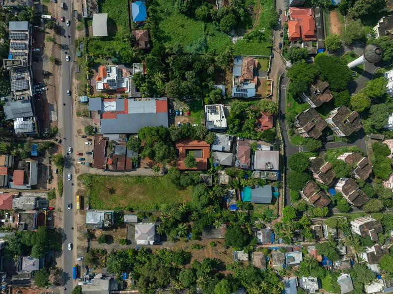 Drone view of dense residential neighborhood showing varied roof colors and tree canopy between houses and streets