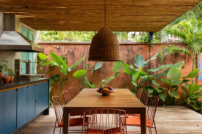 Dining table under woven pendant with weathered copper wall backdrop and banana plants in dappled sunlight
