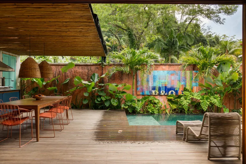 Covered timber deck with pool alongside planted beds and colorful tile mural on boundary wall