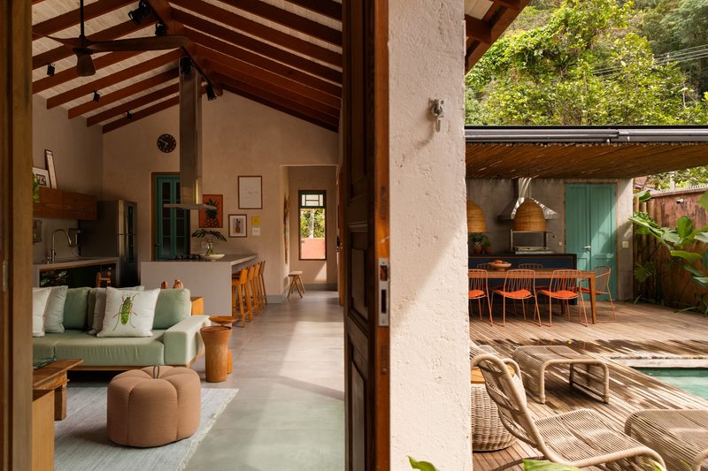 View through open timber door to living area and outdoor deck with pool under dappled sunlight