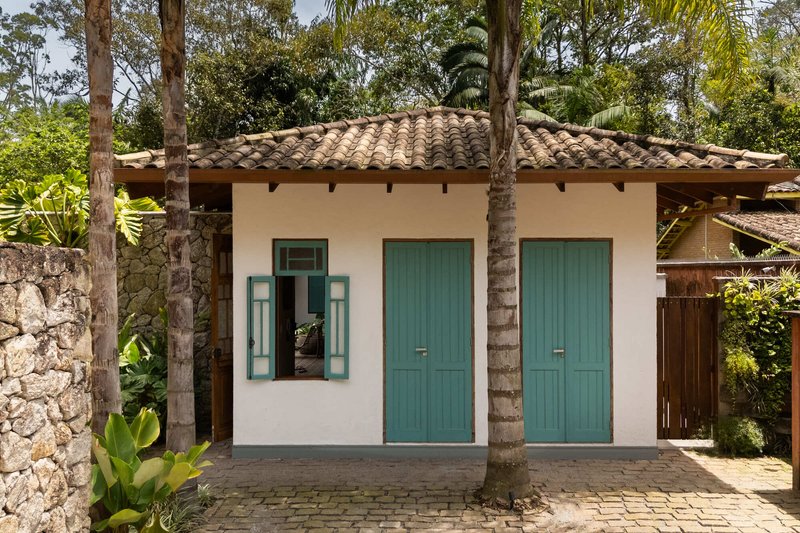 White stucco facade with teal shuttered doors and clay tile roof framed by palms and stone wall