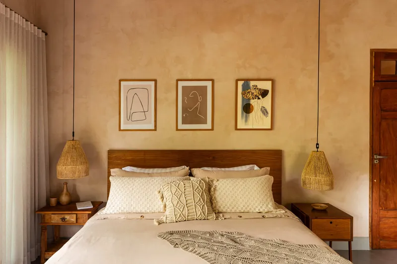 Timber headboard flanked by woven pendant lights and three framed artworks on plaster wall