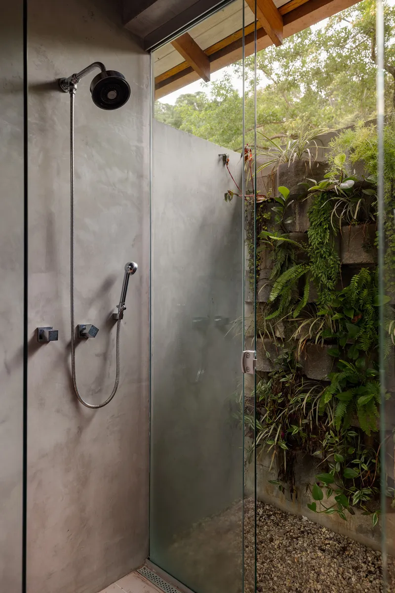 Polished concrete shower enclosure with glass partition opening to planted courtyard with ferns and vines