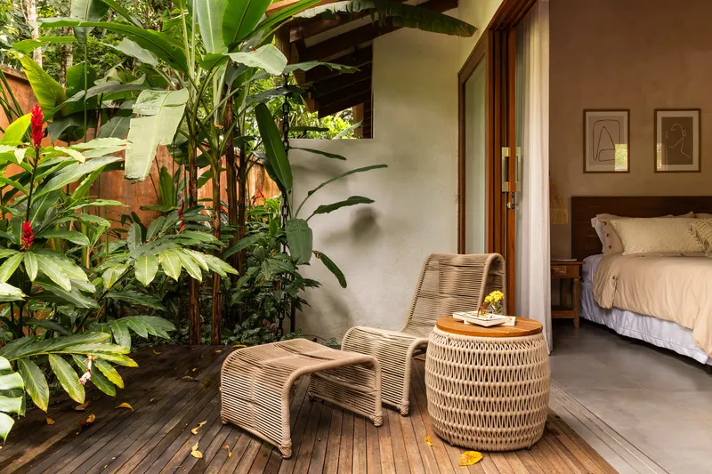 Timber deck terrace with woven lounge chair beside bedroom opening and heliconias in planted bed