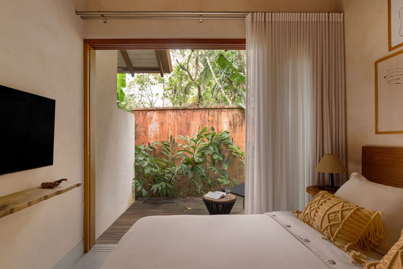 Glass door opening from bedroom to a planted courtyard with weathered copper wall and tropical vegetation