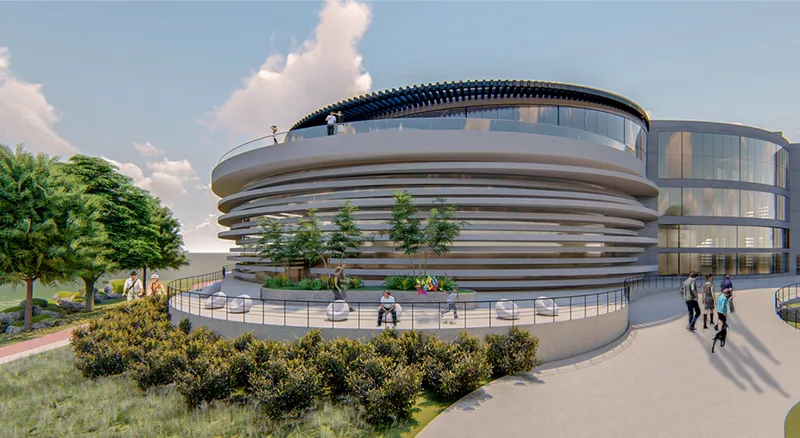 Circular building with horizontal banded facade and rooftop terrace surrounded by landscaped pathways under afternoon clouds