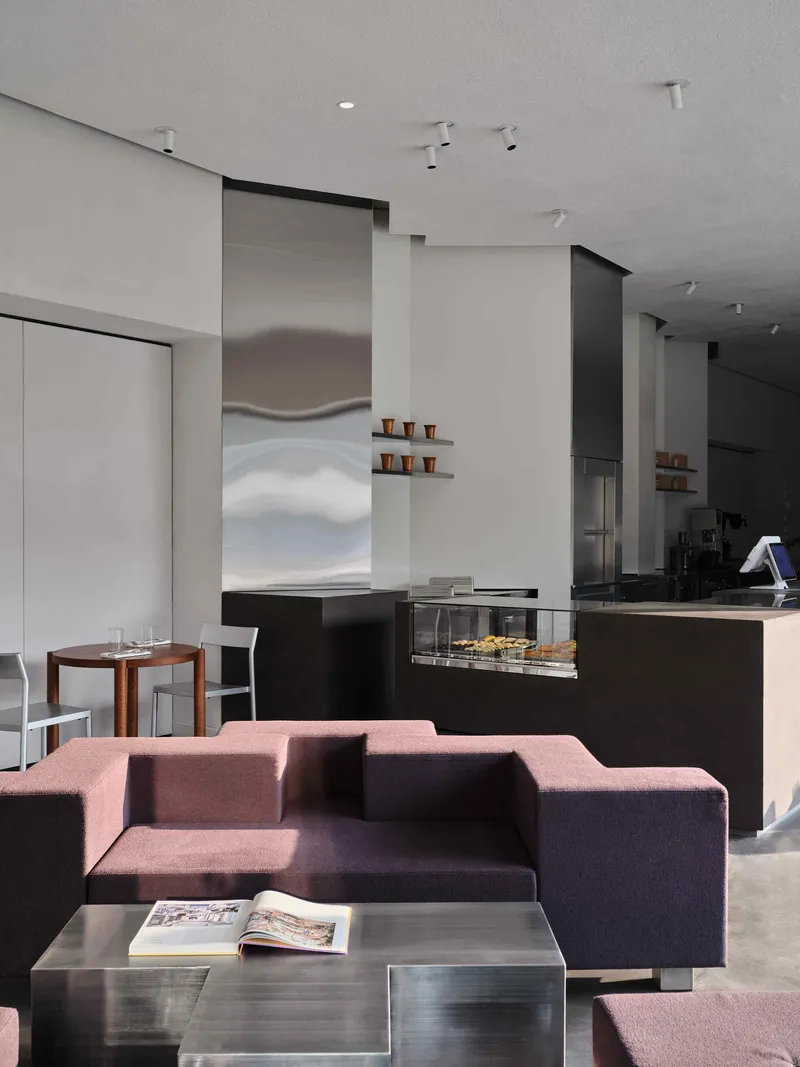 Open-plan space showing the lounge with burgundy seating foreground and black service counter beyond stainless steel column