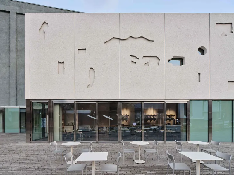 Close-up of the paneled facade with abstract cutouts revealing glimpses of the interior through glazing below