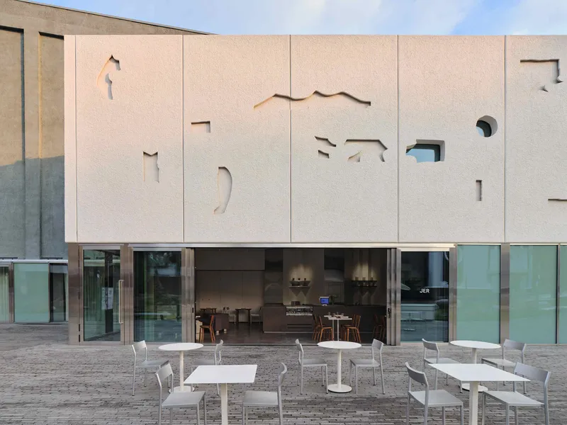 Evening view of the textured facade panels with cutout silhouettes illuminated from within above the glazed entrance