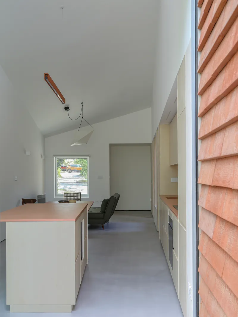 Interior view along kitchen island toward framed window opening with cedar cladding visible outside