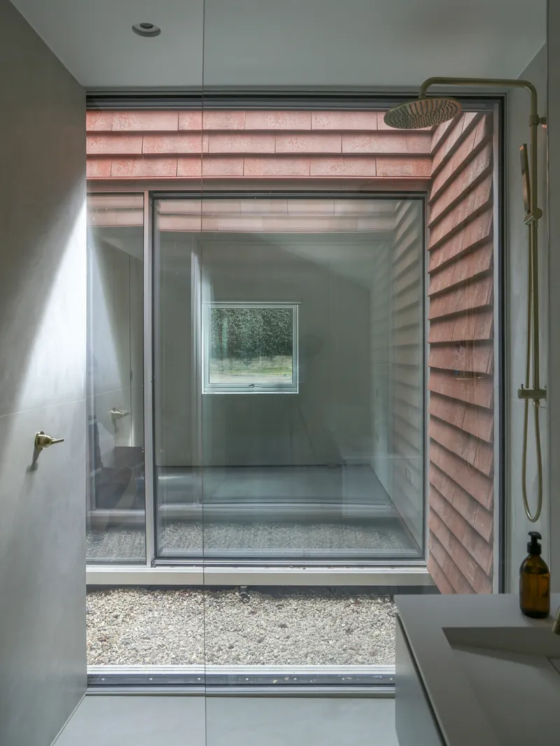 Bathroom with glass-enclosed shower opening to gravel courtyard framed by terracotta tile walls