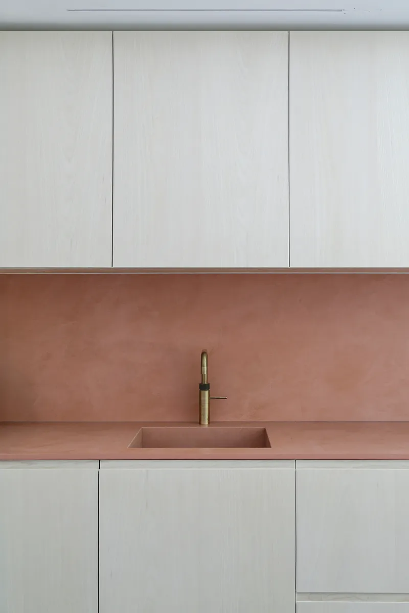 Close-up of copper sink and brass tap set into matching countertop beneath pale timber upper cabinets