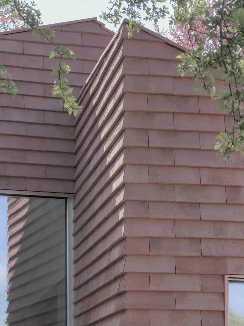 Gabled roof with horizontal timber shingles and deep shadow slot between two volumes