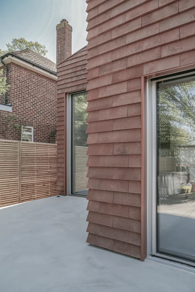 Sloped timber-shingled wall with flush-mounted glazing and timber fence in the background