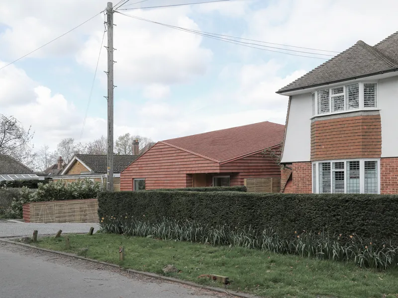 Street view of low-pitched tile roof extension beside brick houses on an overcast day