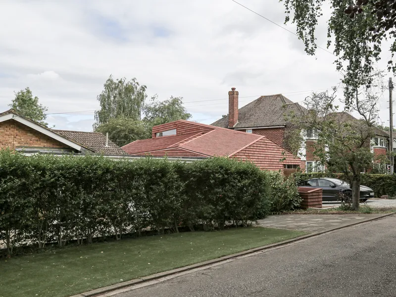 Street view of the ridged terracotta tile extension beside a trimmed hedge and neighboring brick houses