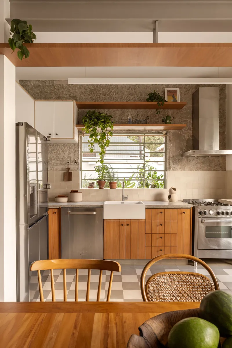 Kitchen counter with timber cabinetry, white farmhouse sink, exposed stone wall, and potted plants on the windowsill