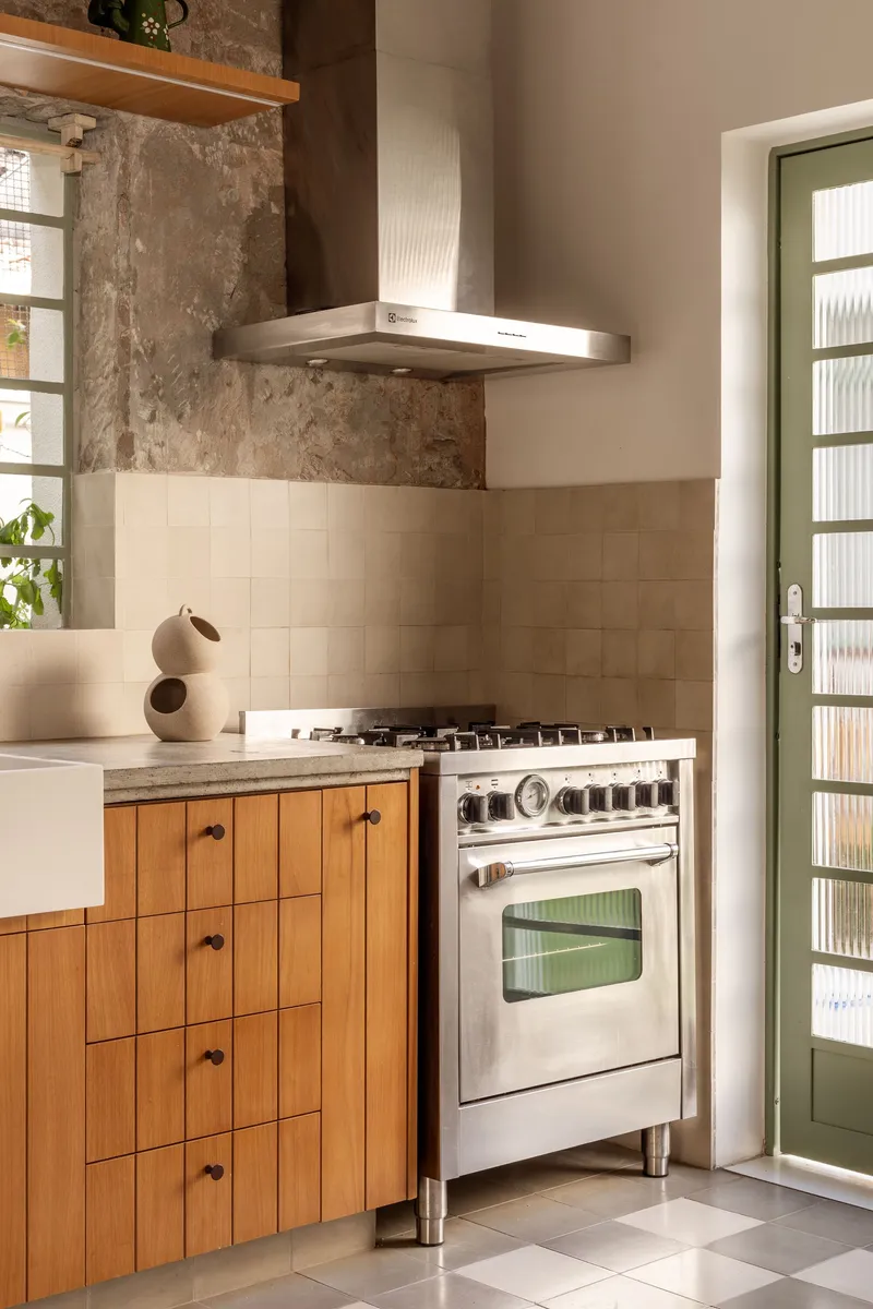 Kitchen cooking zone with freestanding range, stainless hood, timber base cabinets, and exposed weathered wall above